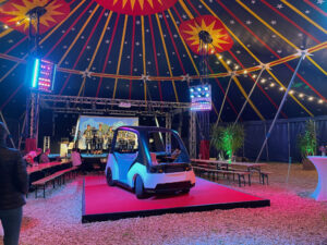 E-Auto auf Bühne in Zirkuszelt, bayerische Blaskapelle im Hintergrund